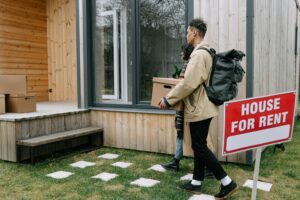 Young couple moving into a new rental home with boxes. Outdoor scene with a rental sign.